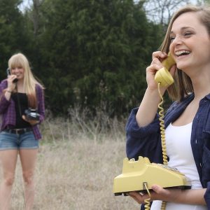 Two young women smiling and talking on old-fashioned rotary phones while standing outside